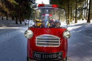 Der mit Kindern vollbesetzte Schneemobilzug Foxi Express fährt durch den verschneiten Wald am Präbichl.