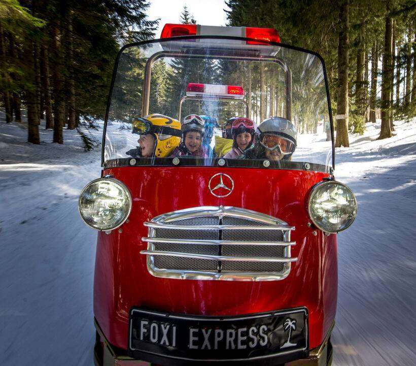 Der mit Kindern vollbesetzte Schneemobilzug Foxi Express fährt durch den verschneiten Wald am Präbichl.