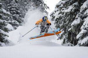 Skifahrer springt im tief verschneiten Wald über eine Welle.