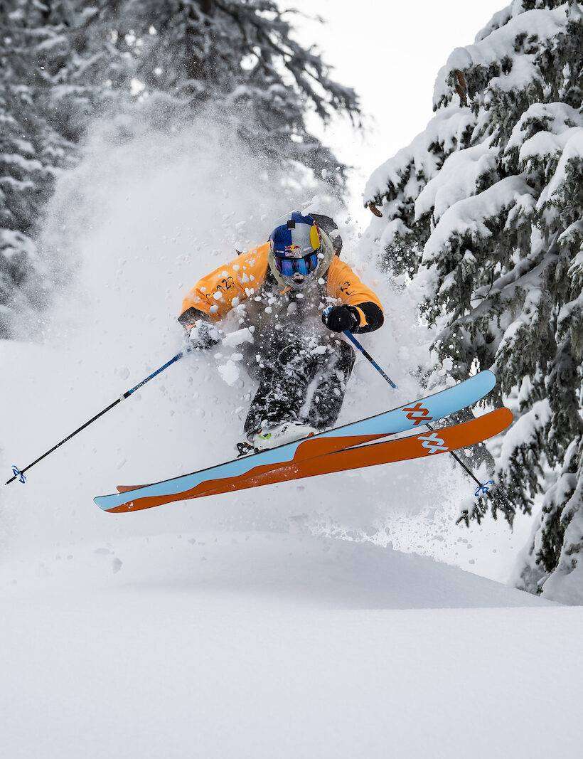 Skifahrer springt im tief verschneiten Wald über eine Welle.