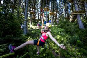 Eine Frau in Klettermontur trägt einen gelben Helm und fliegt im Kletterpark am Präbichl mit der Zipline. Dabei lächelt sie.