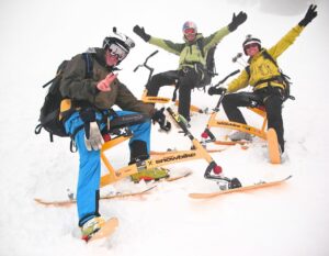 Drei Männer sitzen im Schnee auf Snowbikes und schauen zufrieden in die Kamera.