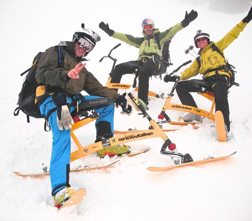 Drei Männer sitzen im Schnee auf Snowbikes und schauen zufrieden in die Kamera.