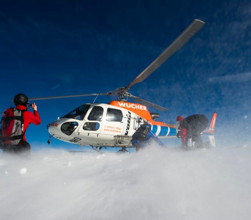 Zwei Leute stehen vor einem laufenden Helikopter, der Schnee aufwirbelt.