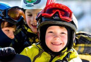 Kinder mit Skihelm und Skibrille lachen in die Kamera