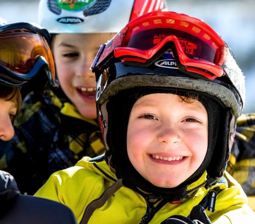 Kinder mit Skihelm und Skibrille lachen in die Kamera