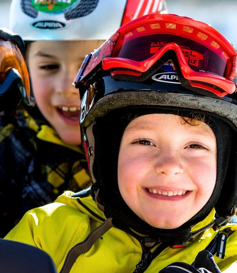 Kinder mit Skihelm und Skibrille lachen in die Kamera